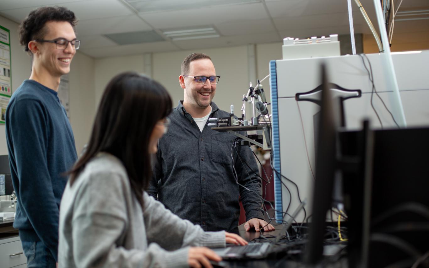 three people stand around a mass spectrometer