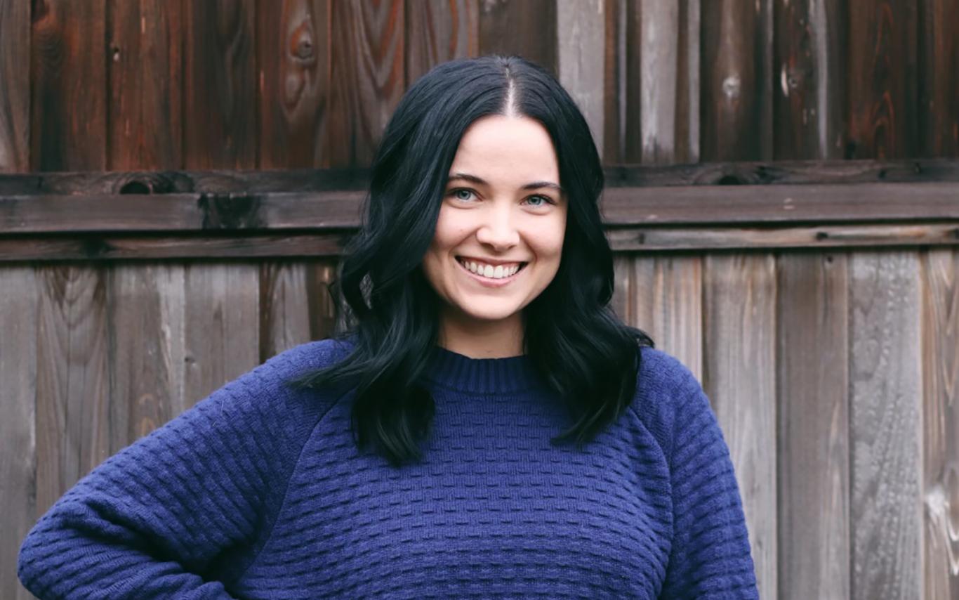 Alisha wearing a blue sweater standing in front of a fence