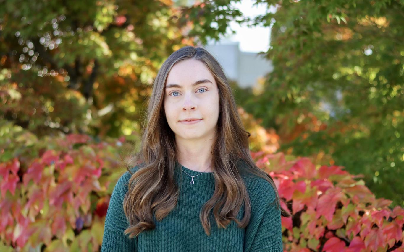 Angelina Jaeger stands in front of a vine covered wall.