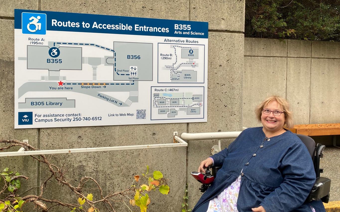 A woman poses beside a wayfinding sign at VIU's Nanaimo campus