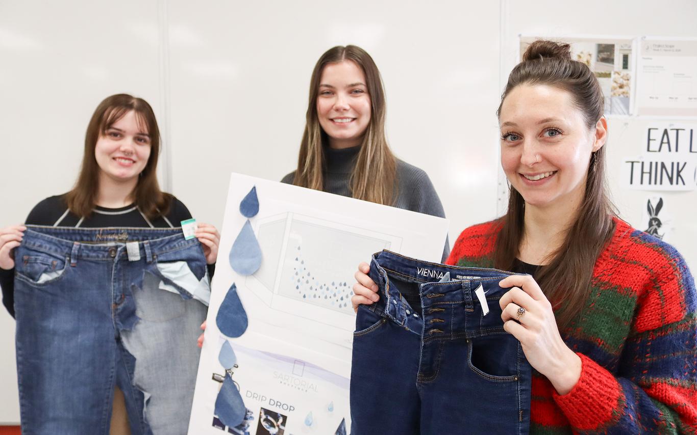 Two students hold up jeans and another holds up a poster.