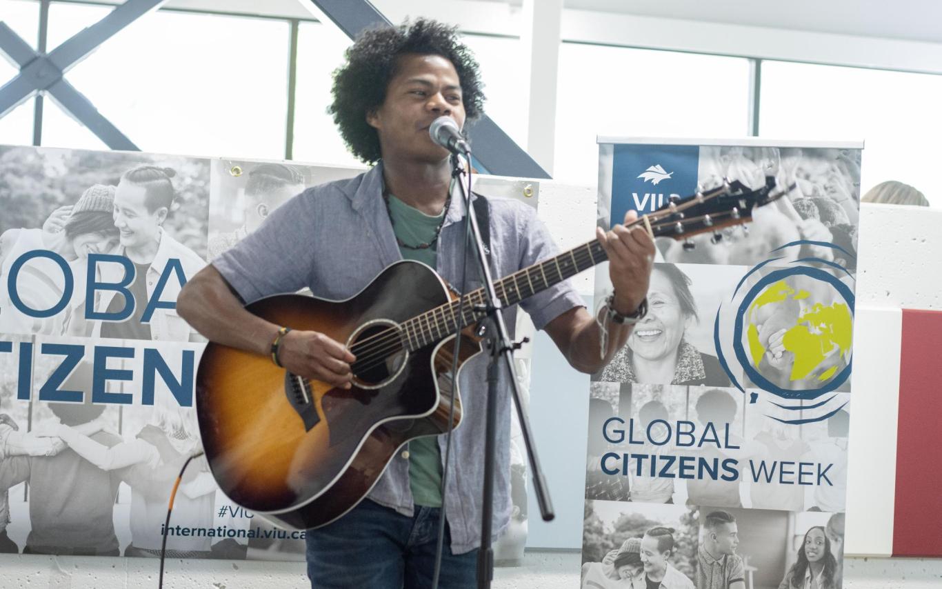 Student sings and plays guitar with Global Citizens Week banners behind him