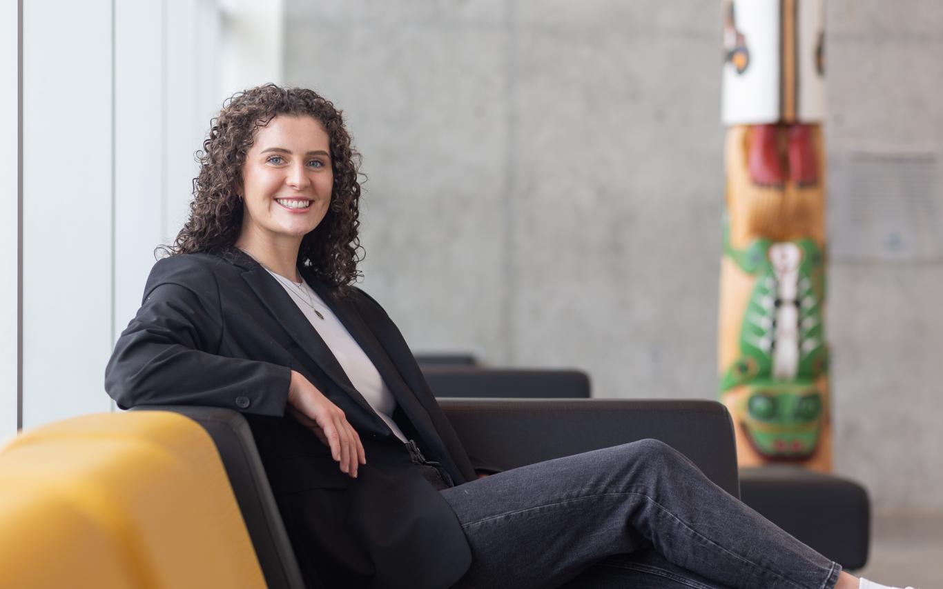 Kayla Passmore sits on a couch in front of the totem in the Centre for Health and Science atrium