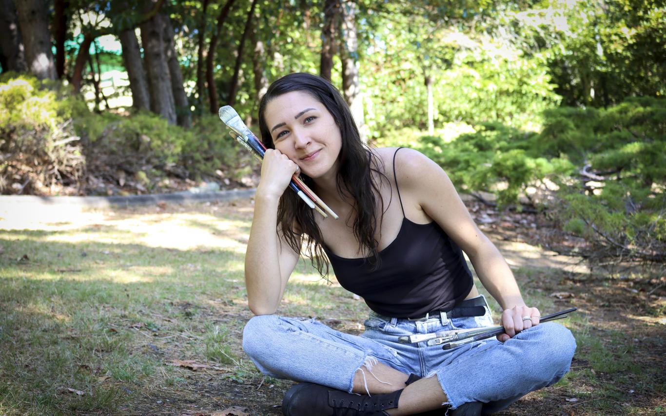 Kashmir Lesnick-Petrovicz sits on the ground and holds paint brushes in her hands.