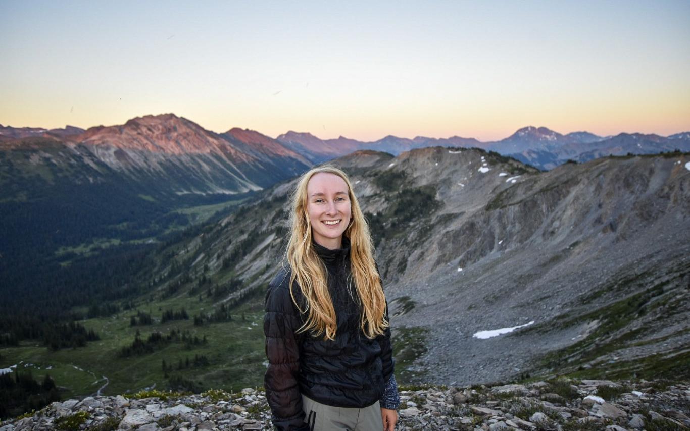 Kelsey Moore smiles with a mountain range at sunset behind her.