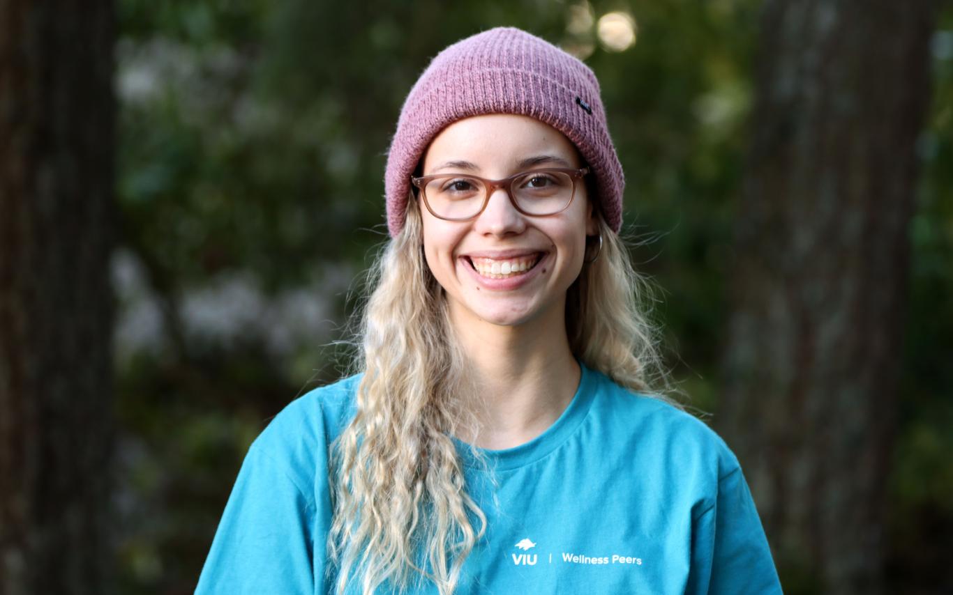 Portrait photo of Kennedy Ordano smiling at the camera with a forest background