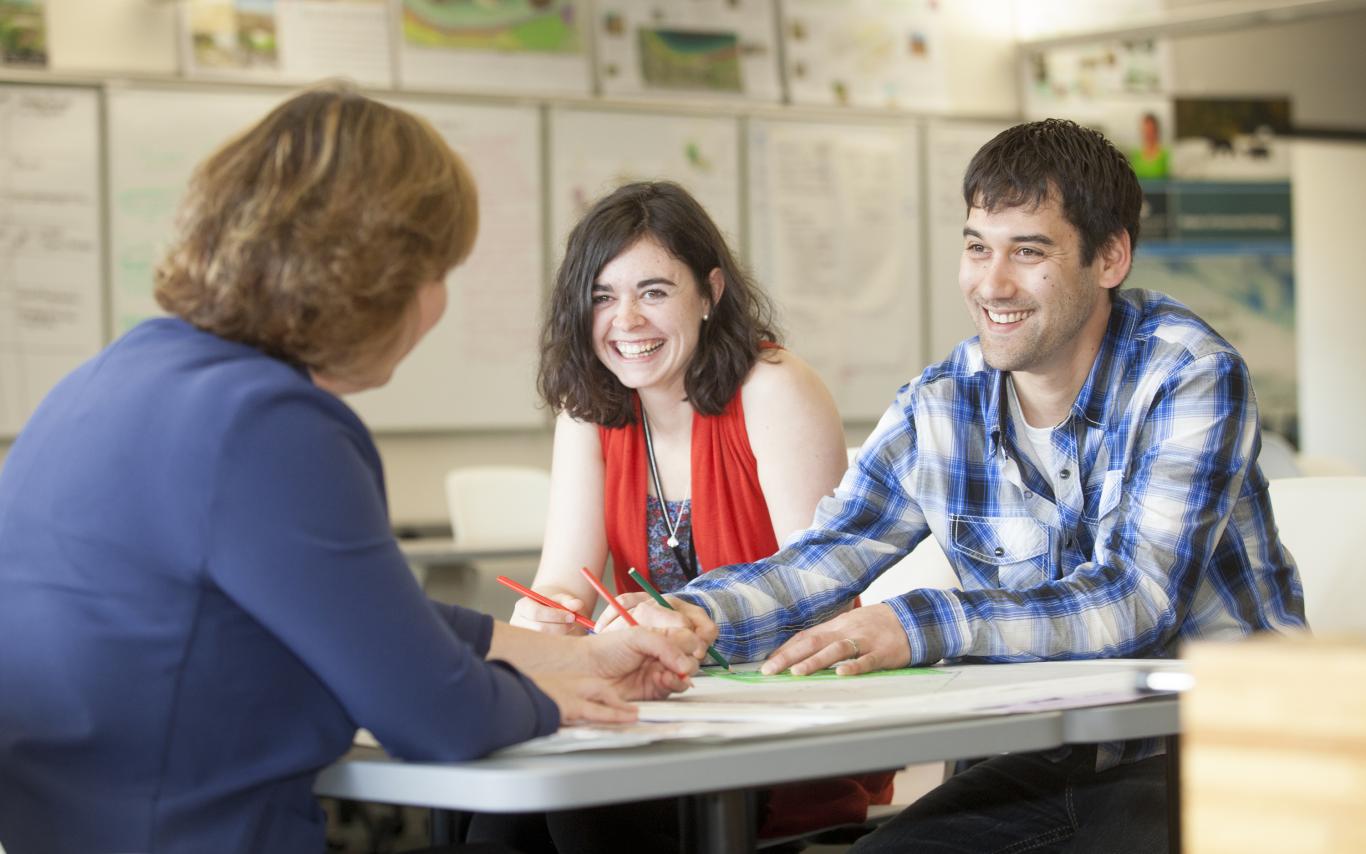 Two graduate students speak with a professor