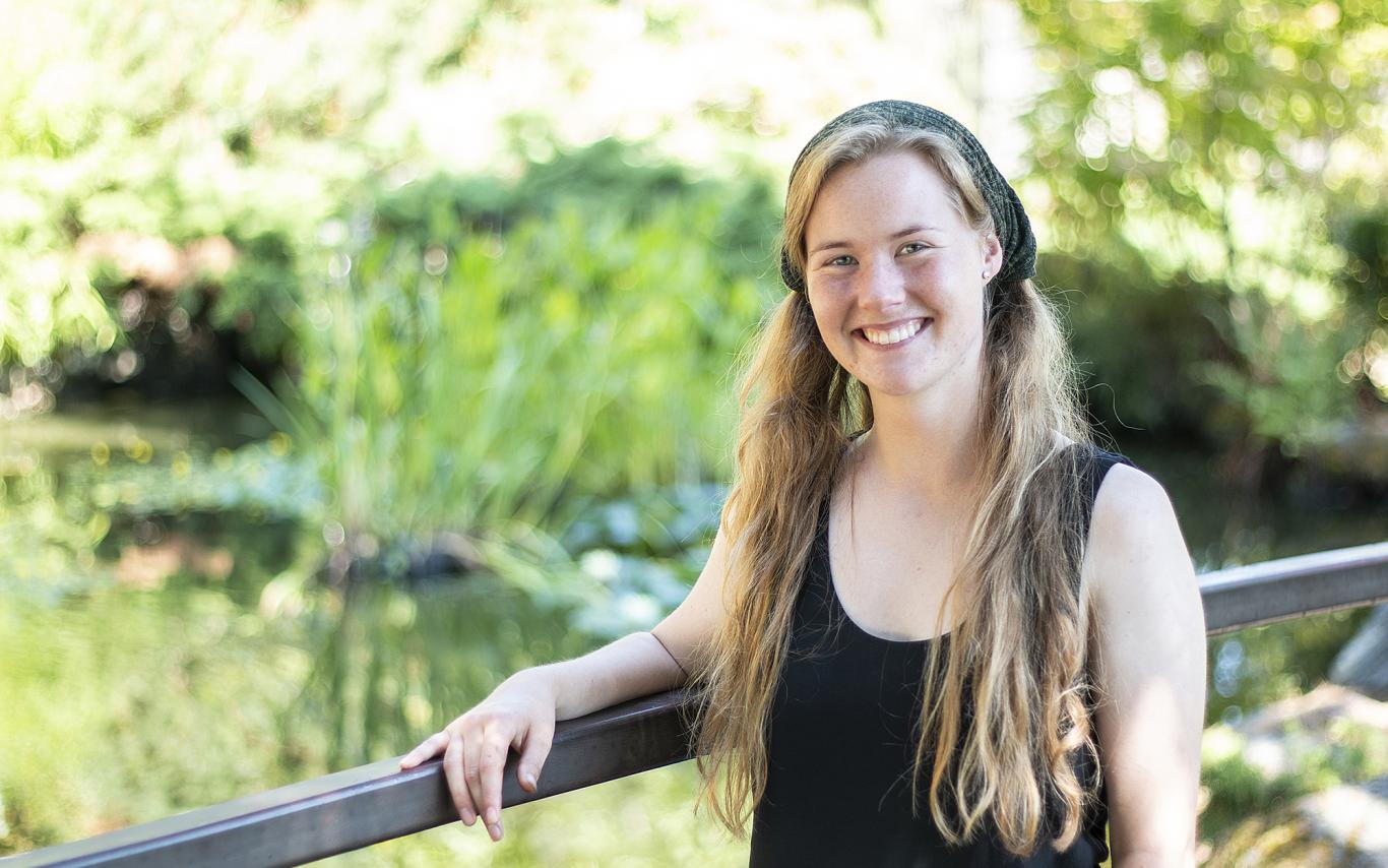 Michaela Medina stands in front of the VIU koi pond, smiling.