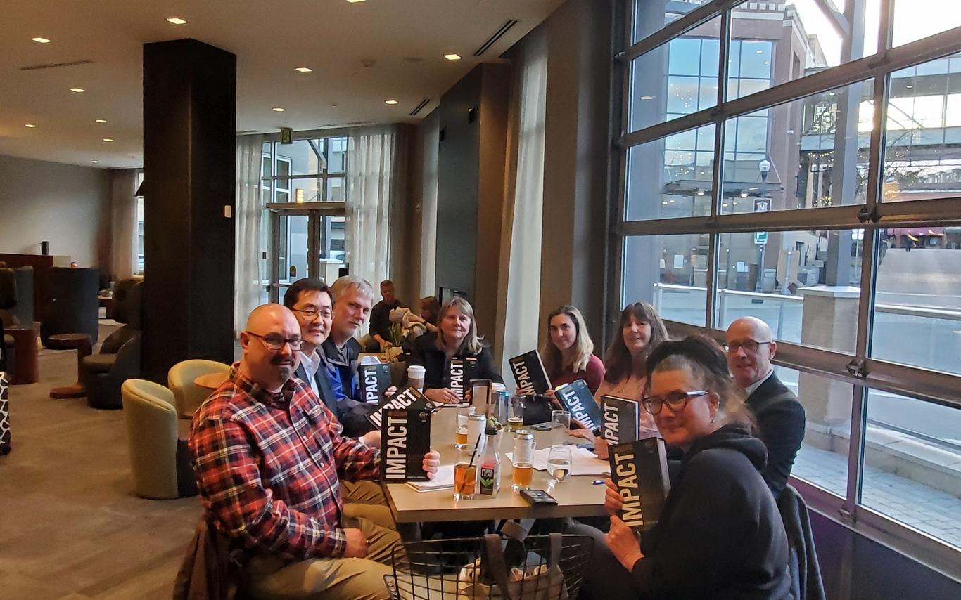 A group of people sit at a table, all holding copies of the same book