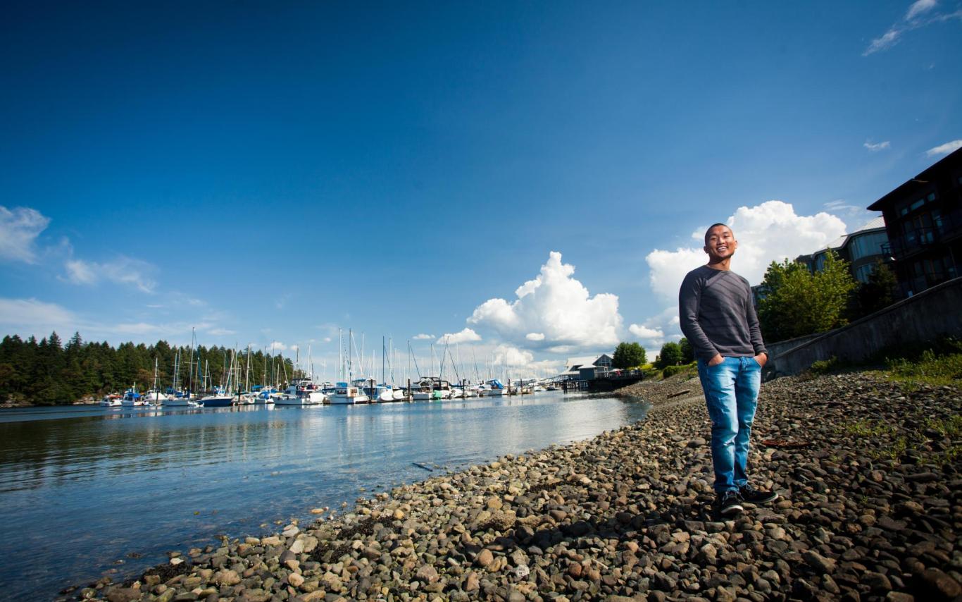 A man stands in the foreground with the waterfront and a marina full of boats behind him