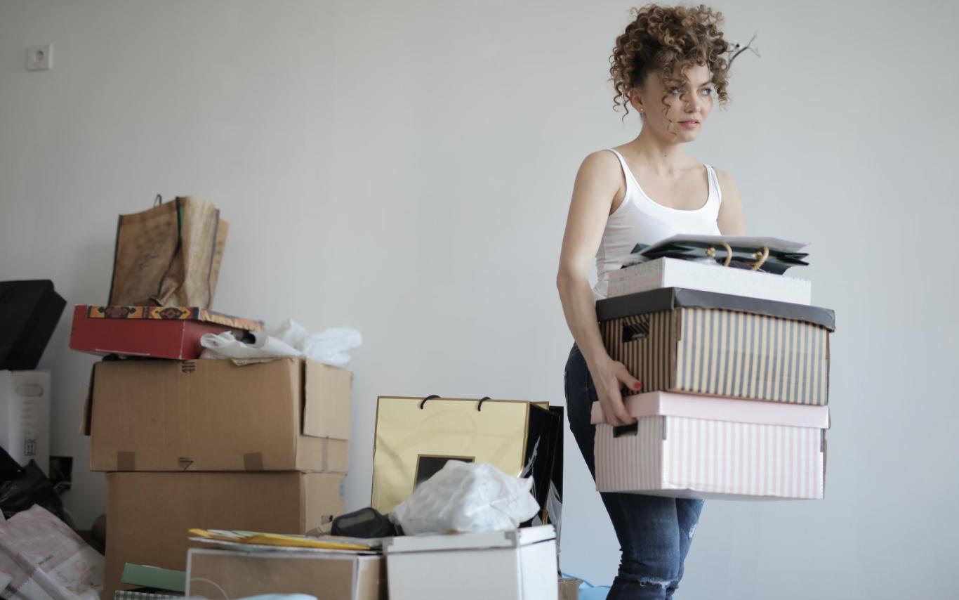 Student carrying boxes with more piled behind her, looking anxious