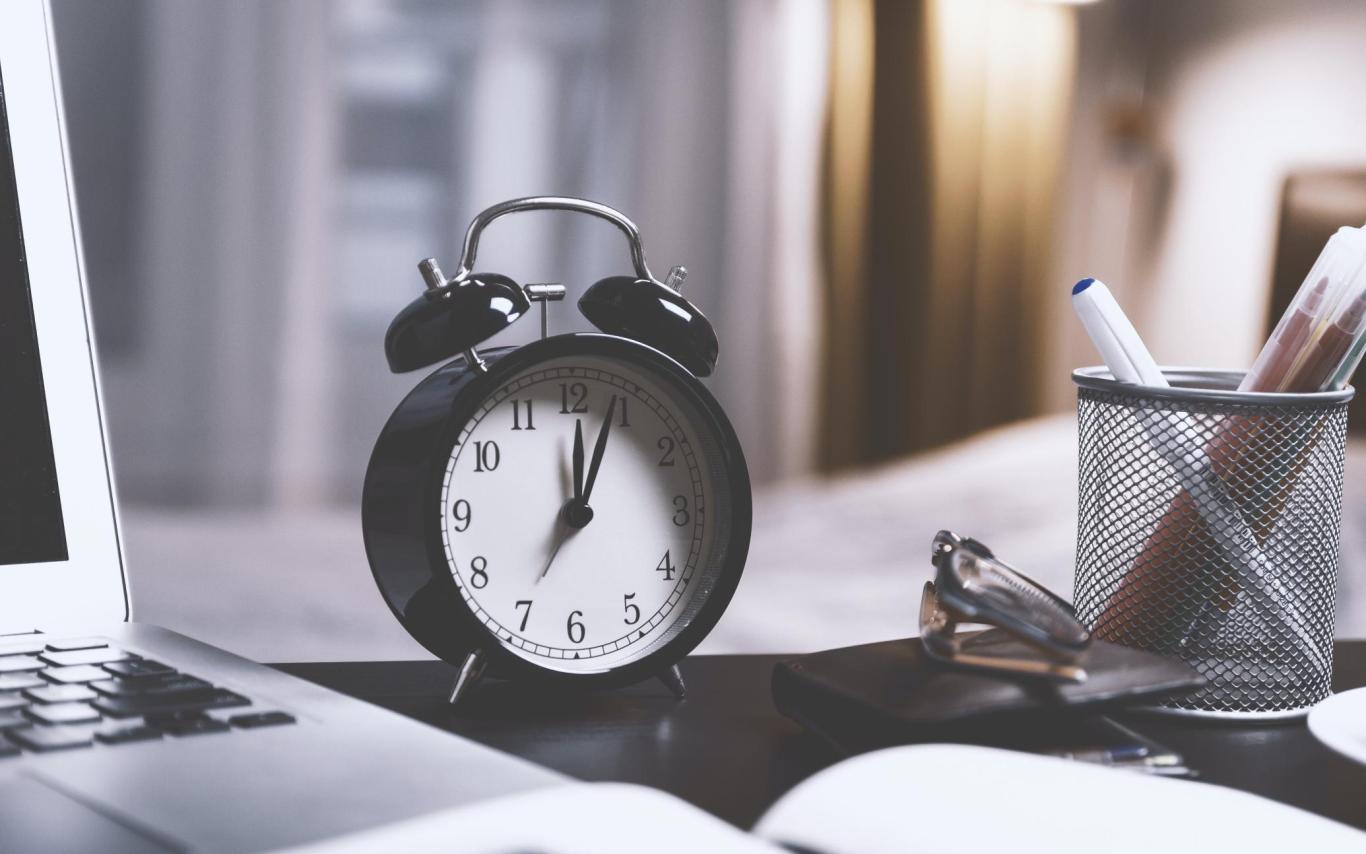 A clock on a desk next to a laptop and pen holder