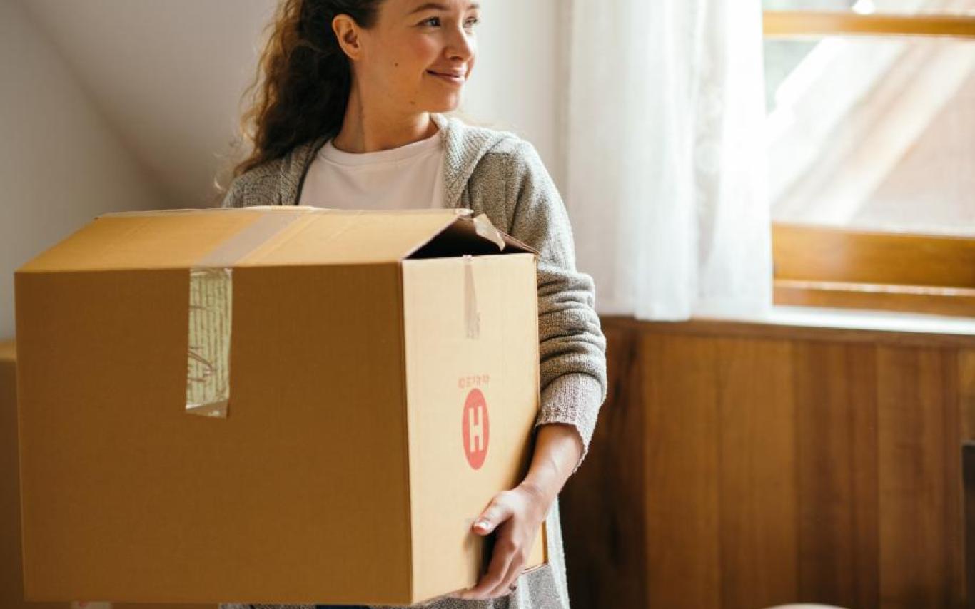 A girl holds a moving box while standing in a bedroom