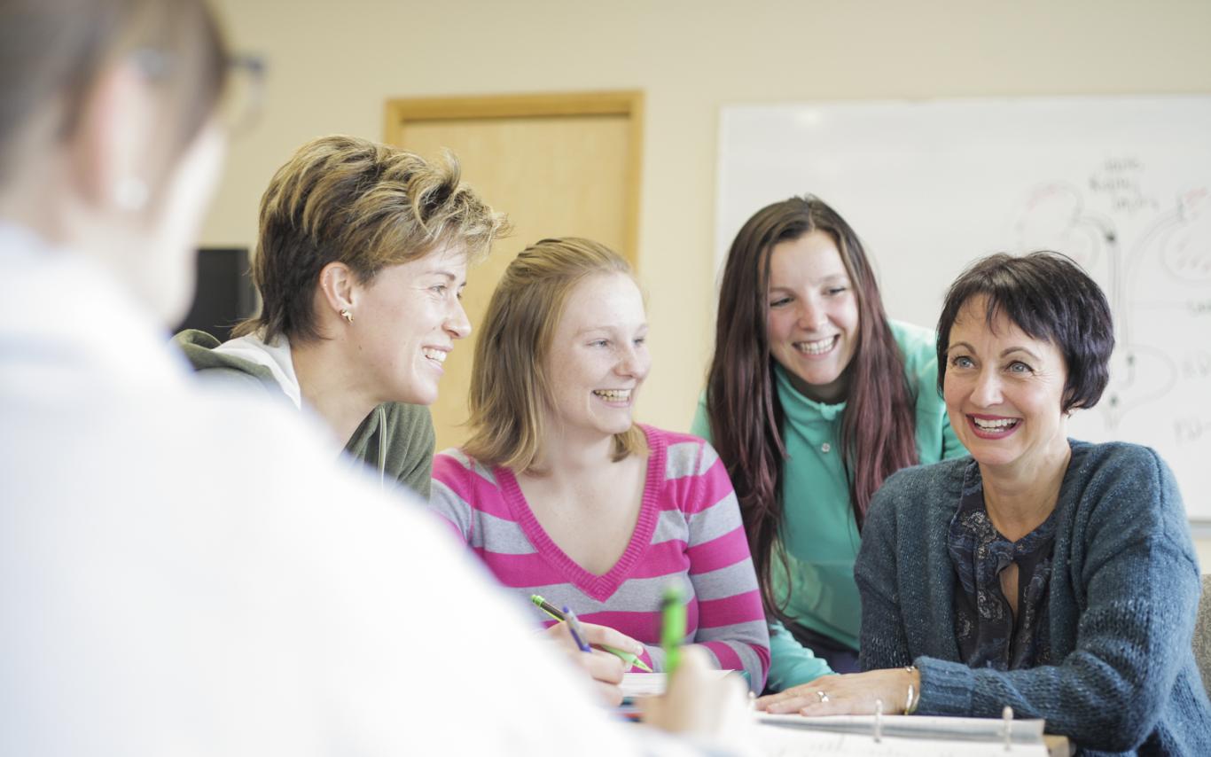 Four students and a faculty member sit at a table together, smiling.