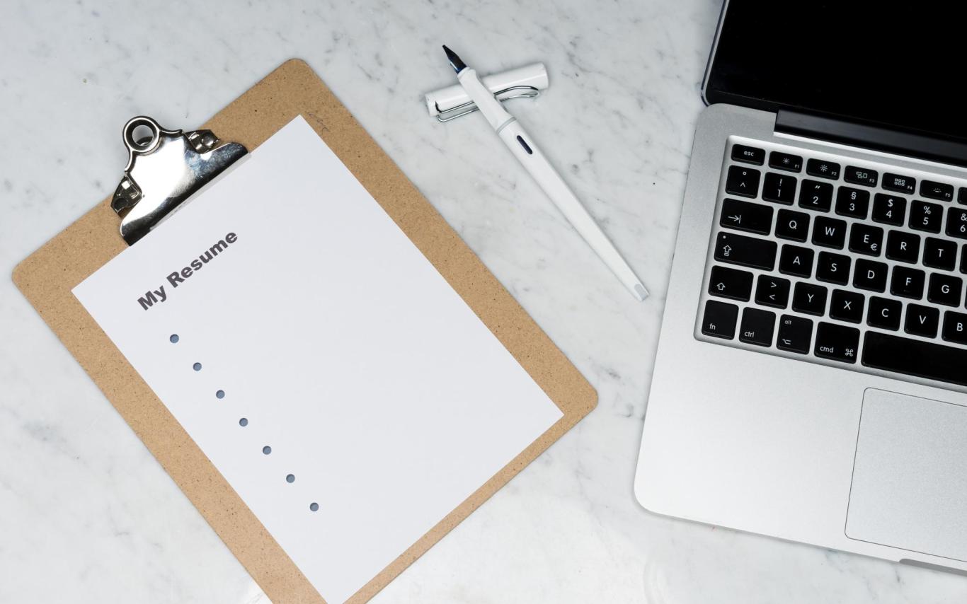 A clipboard the says "My Resume" with bullet points rests next to a laptop 