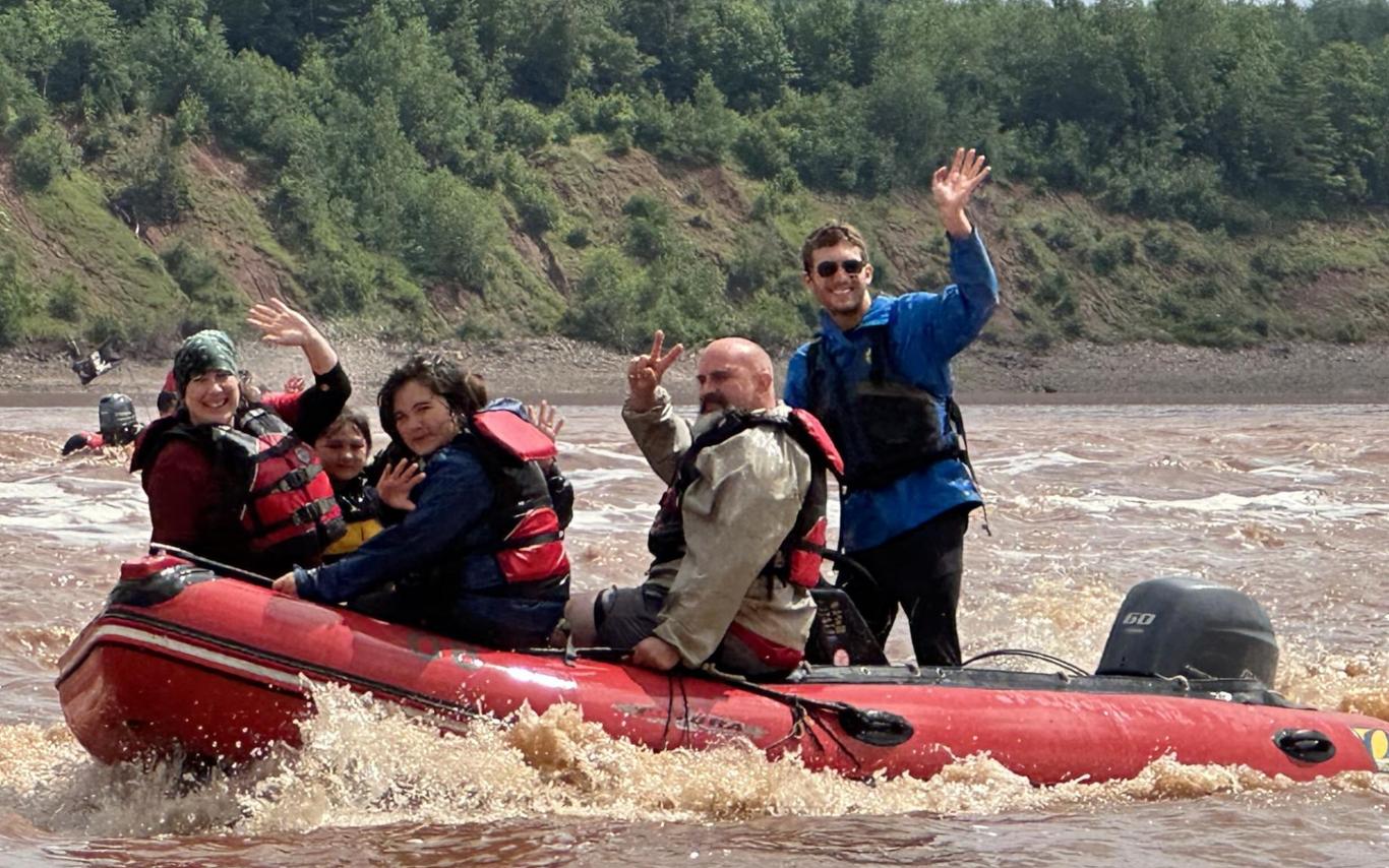 Lucas Gamp in a raft on a river with clients waving at the camera