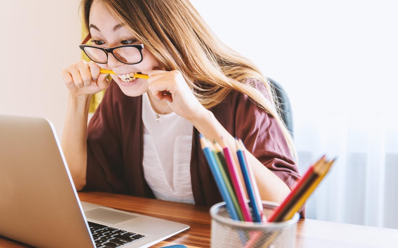 Girl sitting looking at laptop and biting a pencil