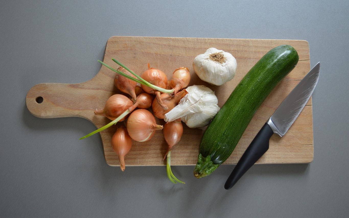 A cutting board with onions, garlic and zucchini