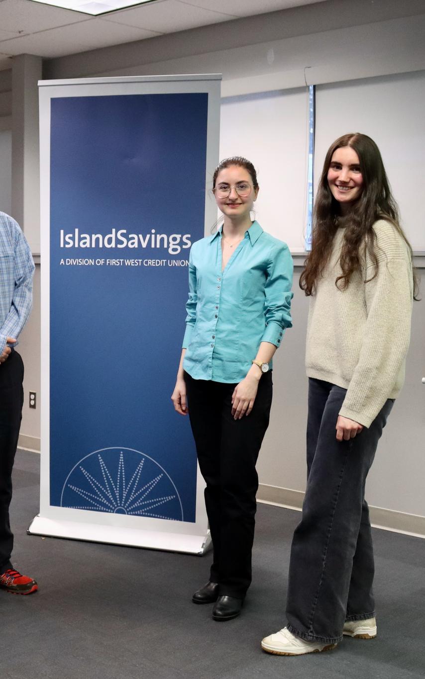 Four students, two males and two females standing beside a banner