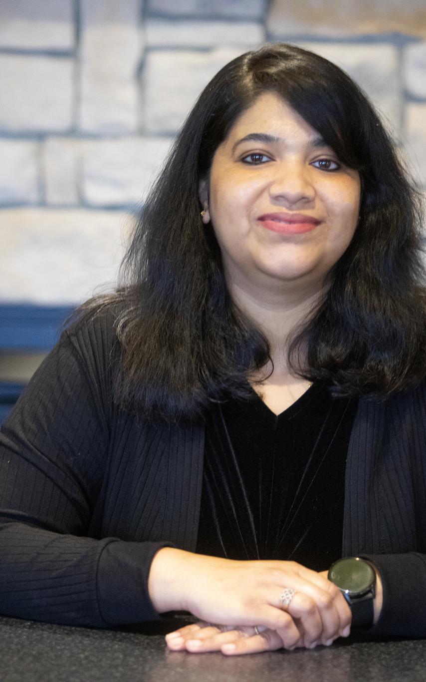 A woman sits at a desk with a stone wall behind her