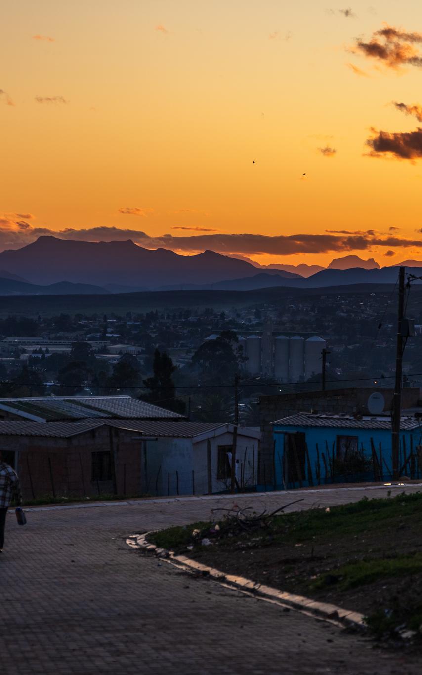 The township of Zolani at sunset. The sky is a light orange while the foreground is cast in shadow.